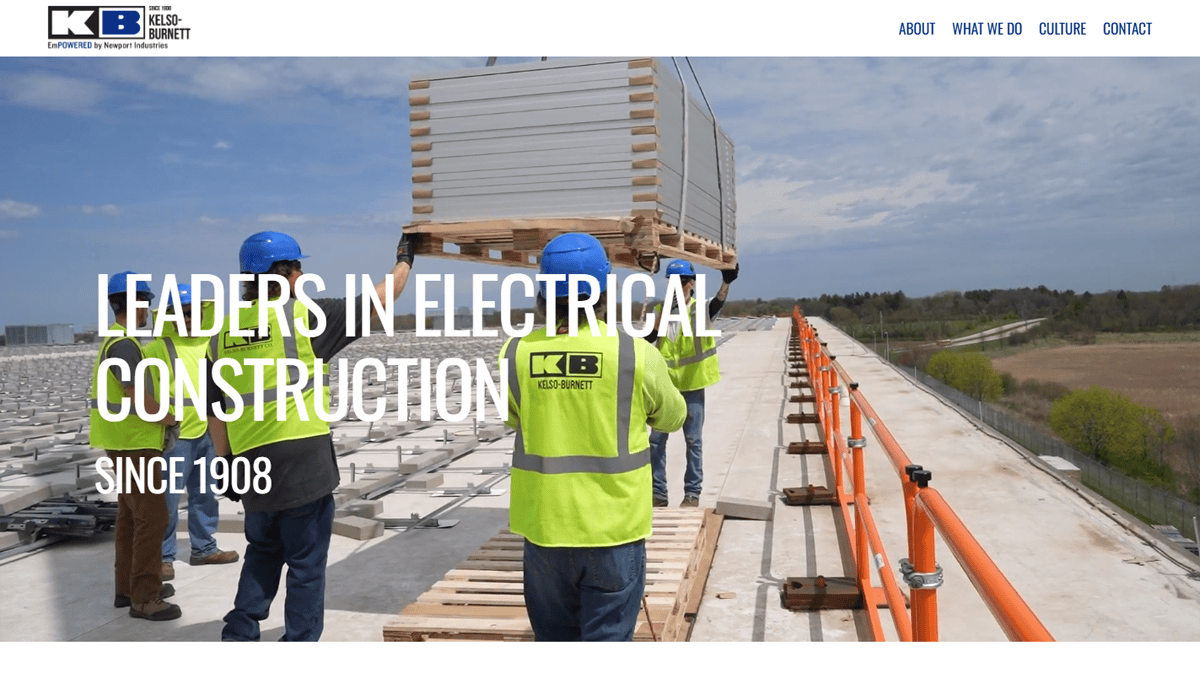 Workers in safety gear guide a crane lifting materials on a rooftop construction site. The text reads Leaders in Electrical Construction Since 1908—your trusted commercial electrician. Blue sky and trees are in the background.