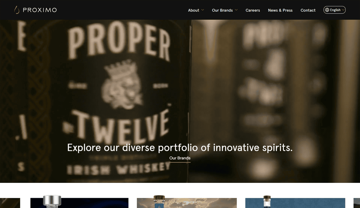 A blurred close-up of a Proper No. Twelve Irish Whiskey bottle label, highlighting user engagement and “Explore our diverse portfolio of innovative spirits,” with a navigation menu at the top of the Proximo Spirits beverage distributor website design homepage.