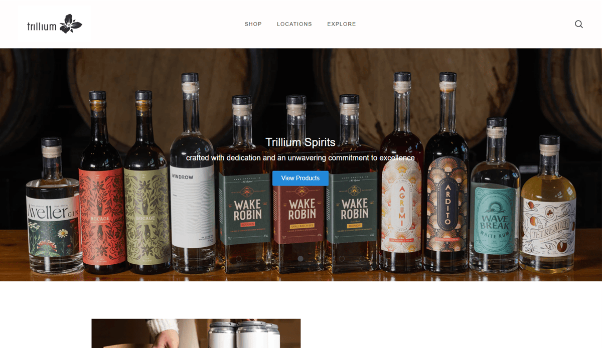 A row of assorted Trillium Spirits bottles displayed on a wooden surface, with barrels in the background. The website banner showcases “Trillium Spirits” and “View Products,” reflecting the latest brewery website design trends.