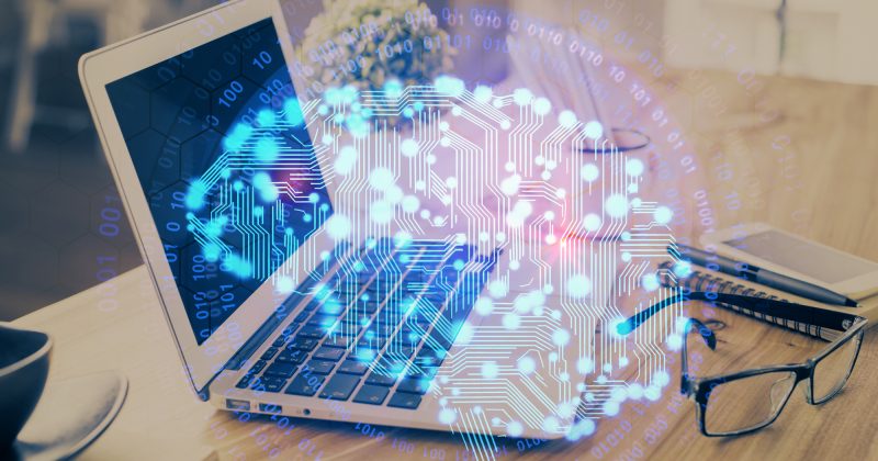 A laptop on a desk with glasses and a cup, overlaid with a glowing digital brain and binary code, symbolizing the innovative intersection of artificial intelligence and technology—perfect for showcasing cutting-edge AI Websites or dynamic WordPress Websites.